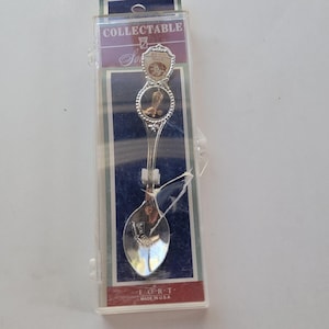 May include: A silver-colored collectible spoon in a clear plastic case. The spoon features a decorative handle with a crest and a detailed bowl. The packaging reads "COLLECTABLE" and "FORT MADE IN U.S.A."