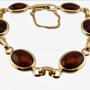 May include: A gold-toned bracelet featuring oval-shaped, reddish-brown stones. The bracelet has a delicate chain for closure and is composed of multiple linked segments. The stones are set in gold bezels.