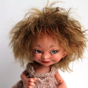 Könnte beinhalten: Eine handgefertigte Puppe mit braunen Haaren und einem schelmischen Ausdruck. Die Puppe trägt ein gestricktes Kleid und hat gemalte Sommersprossen im Gesicht.