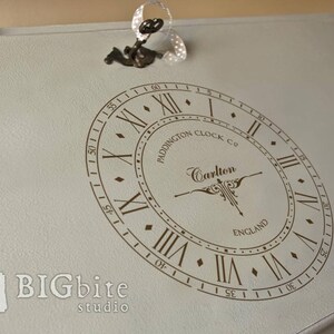 May include: A vintage-style clock face with Roman numerals and the text "Paddington Clock Co. Carlton England" in a brown font on a light gray background.