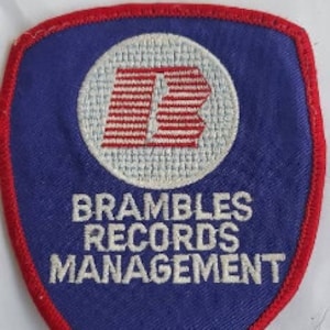 May include: A blue and red embroidered patch with the text "Brambles Records Management" and a stylized letter "B" in the center.