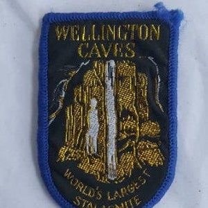 May include: A blue and black embroidered patch with gold lettering that reads "Wellington Caves, World's Largest Stalagmite".