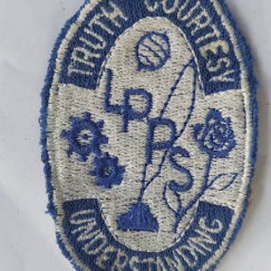 Puede incluir: Parche bordado azul y blanco con el texto "Truth Courtesy Understanding" y el acrónimo "L.P.D.S." en el centro.