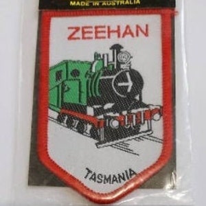 May include: Red, white, and green embroidered patch with a cartoon train and the text "Zeehan Tasmania".