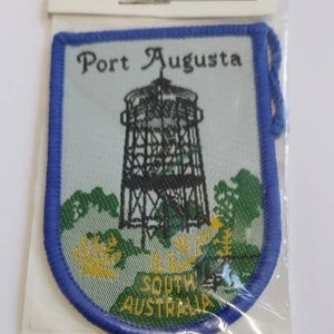 Puede incluir: Parche bordado azul y blanco con el texto "Port Augusta" y "South Australia". El parche presenta una ilustración en blanco y negro de una torre de agua.