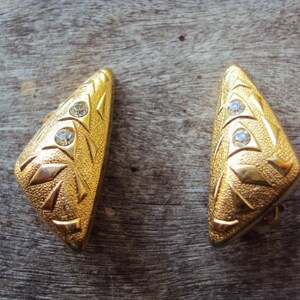 Könnte beinhalten: Ein Paar goldfarbene Ohrringe mit geometrischem Design und klaren Strasssteinen.