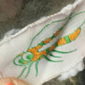 Pode incluir: Remendo de tecido branco com um desenho de libélula bordado em verde e laranja.