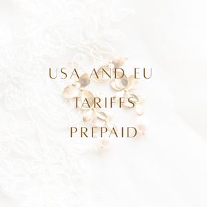 K&ouml;nnte beinhalten: Goldfarbene Ohrh&auml;nger mit zarten bl&uuml;tenf&ouml;rmigen Elementen und kleinen wei&szlig;en Perlen an der Unterseite. Der Text USA AND EU TARIFFS PREPAID ist &uuml;ber das Bild gelegt. Die Ohrringe haben eine polierte Oberfl&auml;che und Hakenverschl&uuml;sse.