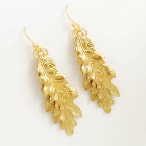May include: A pair of gold-tone earrings featuring a detailed oak leaf design. The leaves are layered and have a textured finish.
