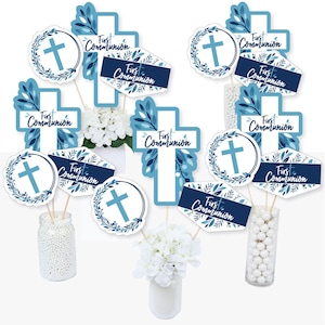 May include: Blue and white First Communion party decorations with cross and floral designs. The decorations include a cross, a wreath with a cross, and a banner with the words "First Communion".