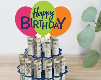 May include: A blue and white cake stand with rolled up dollar bills in each tier. The stand is decorated with white polka dots and has a blue base. The top of the stand has three balloons in the colors green, pink, and orange with the words "Happy Birthday" written in black.