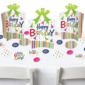 May include: A set of colorful birthday party table decorations. The centerpiece is a large, white gift box with a green bow and the words "Happy Birthday" in red, blue, and yellow. There are also smaller, round confetti pieces with various birthday-themed designs.
