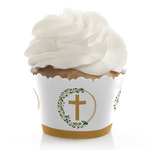 May include: White cupcake with white frosting in a white cupcake wrapper with a gold and green design featuring a cross in a wreath.