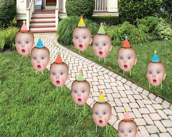 Puede incluir: Nueve recortes de cartón coloridos de caras de bebés con sombreros de fiesta. Los recortes se colocan en un césped verde con un camino de ladrillos.