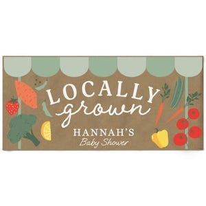 May include: A rectangular sign with a brown background and a light green scalloped awning design at the top. It features the text LOCALLY grown HANNAH'S Baby Shower in white, surrounded by illustrations of strawberries, broccoli, carrots, and tomatoes.