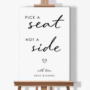 May include: A white sign on a wooden easel with black text that reads "Pick a seat not a side" with a heart symbol and the words "with love, Emily & Daniel".