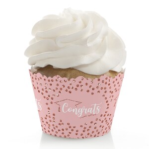 May include: A cupcake with white frosting in a pink wrapper. The wrapper has a scalloped edge and is decorated with rose gold confetti and the word "Congrats" with a graduation cap graphic.
