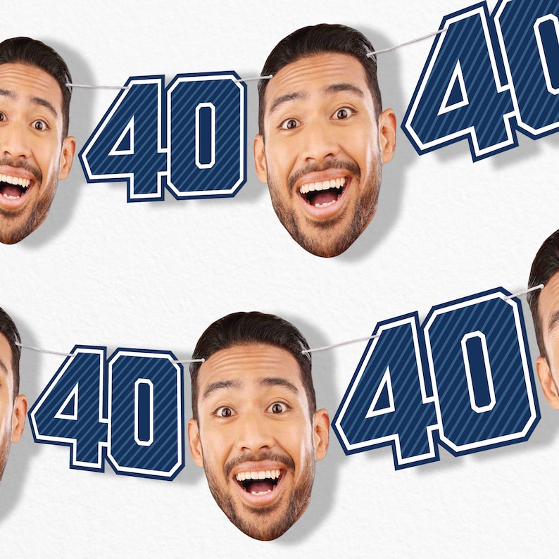 May include: A banner with the number "40" in navy blue with white trim, strung between smiling faces of a man. The banner is against a white background. The man has dark hair and a beard, and is smiling with his mouth open.