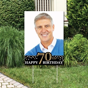May include: A black and gold 70th birthday yard sign with a photo of a person. The sign has gold glitter accents and white polka dots.