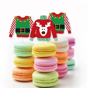 Puede incluir: Imagen festiva con coloridos macarons apilados en torres, coronados con adornos en forma de su&eacute;ter navide&ntilde;o. Los adornos son rojos y verdes con dise&ntilde;os navide&ntilde;os, incluyendo un reno y un su&eacute;ter de elfo. Los macarons son de varios colores.