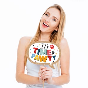 May include: A woman holds a brown cardboard photo booth prop with a speech bubble shape. The speech bubble says "It's Time to Pawty" in colorful letters with a paw print.