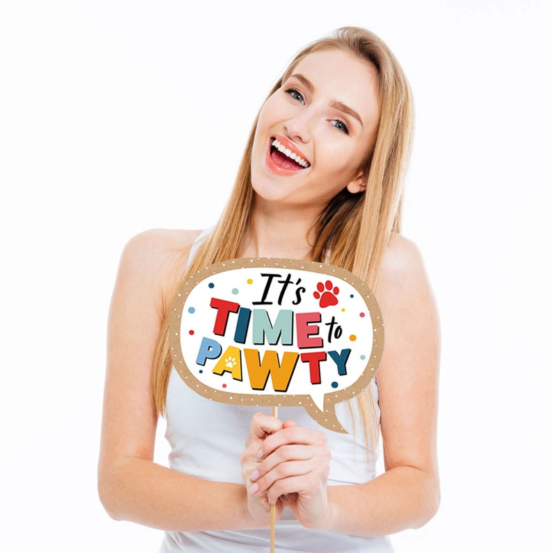 May include: A woman holds a brown cardboard photo booth prop with a speech bubble shape. The speech bubble says "It's Time to Pawty" in colorful letters with a paw print.