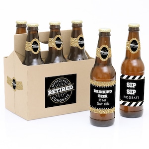 May include: A six-pack of beer bottles in a cardboard carrier. The bottles have gold glitter labels and the text "Drinking beer is my day job" and "Sip Sip Hooray!". The carrier has a label that says "Officially Retired Congrats".
