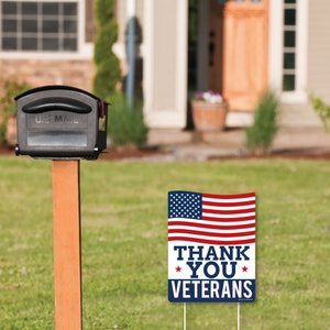 Puede incluir: Una bandera estadounidense roja, blanca y azul con las palabras "Thank You Veterans" impresas en ella. La bandera est&aacute; en una estaca de madera y est&aacute; en un jard&iacute;n de c&eacute;sped.