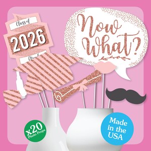 May include: A collection of 20 photo props in a pink and rose gold color scheme. Props include speech bubbles with the text "Now What?", a mustache, lips, graduation cap, diploma, and signs that say "Class of 2026".