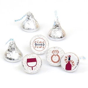 May include: Six silver foil-wrapped chocolate candies. Two are upright cones with paper plumes. Four are flat-bottomed with circular labels featuring a wine glass, a diamond ring, a wine bottle, and the text "vino before vows" in rose gold.