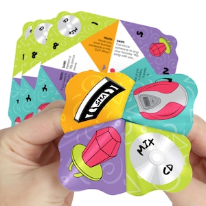 May include: A colorful, multi-sided spinner game with a 90s theme. The spinner has five sides, each with a different design and text. The sides include a CD, a ring, a boombox, a cassette tape, and a question mark. The text on the spinner includes "Mix CD", "Truth", "Dare", "Track 0", and "SHA!"