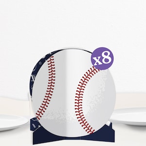 May include: Baseball-themed party decorations. A white baseball with red stitching is the focal point, set against a navy blue base. A purple circle with the number "x8" indicates the quantity. The design is suitable for a baseball-themed event.