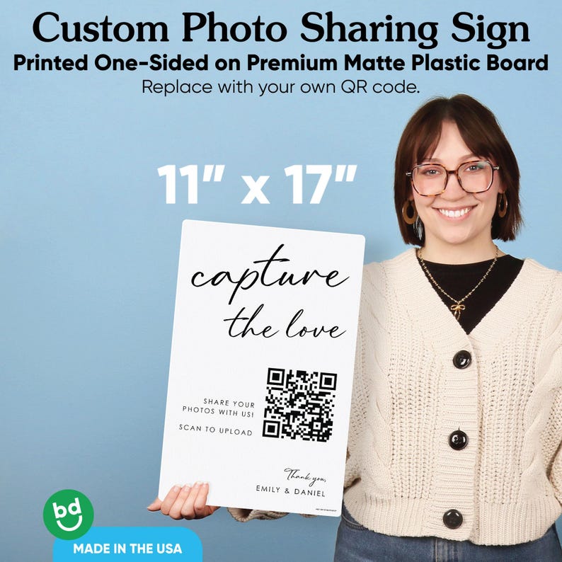 May include: A white rectangular matte plastic sign measuring 11 inches by 17 inches. The sign features the black text capture the love, a QR code, the text SHARE YOUR PHOTOS WITH US! SCAN TO UPLOAD, and the text Thank you, EMILY & DANIEL.