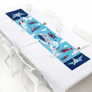May include: A blue and red airplane themed table runner with the text "Time Flies" on a white background. The runner is decorated with red airplanes, white clouds, and blue stars.
