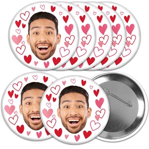 May include: Set of six 2.25 inch round button pins featuring a smiling man's face surrounded by pink and red hearts. The buttons are white with a silver backing.