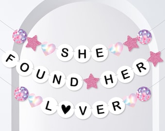May include: A white banner with the words "She Found Her Lover" in black letters. The banner is decorated with pink glitter stars, iridescent hearts, and disco ball ornaments.
