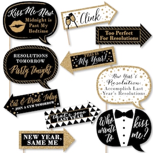May include: A collection of black and gold photo booth props with various phrases for a New Year's Eve celebration. The props include speech bubbles and arrows with text like "Kiss Me Now," "Party Tonight," and "New Year, Same Me."