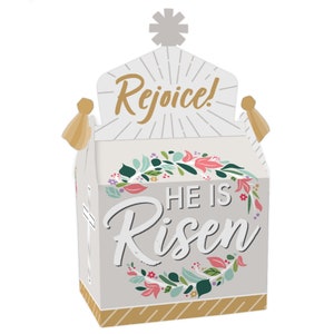 May include: A white and gold Easter favor box with a church design. The box has a floral wreath with the text "He is Risen" and the words "Rejoice!" on the top.