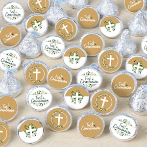 May include: A collection of chocolate kiss candies decorated with round stickers featuring a gold cross and green leaves. The stickers say "First Communion" in a gold script font.
