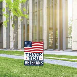 Puede incluir: Una bandera estadounidense roja, blanca y azul con las palabras "Thank You Veterans" impresas en ella. La bandera se muestra en un cartel de jard&iacute;n.