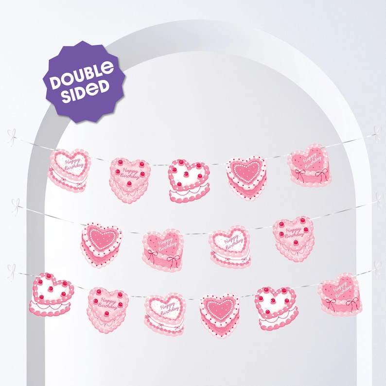 May include: A pink heart-shaped banner with the words "Happy Birthday" on some of the hearts. The banner is double-sided and has a cake design with white frosting and red cherries. The banner is strung on a white string.