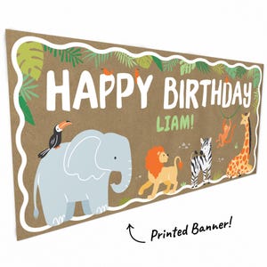 May include: A rectangular banner with a brown background and white border. The banner reads "HAPPY BIRTHDAY LIAM!" in large white letters. Cartoon animals, including an elephant, lion, zebra, and giraffe, are featured. A toucan and monkey are also present. The banner is a printed product.
