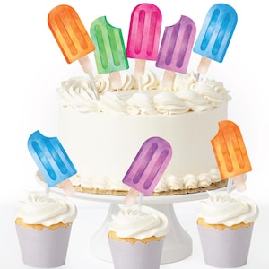 May include: A white frosted cake and cupcakes are decorated with colorful popsicle-shaped toppers. The toppers are in shades of orange, green, pink, purple, and blue. The cake sits on a white cake stand, and the cupcakes are in gray paper cups.