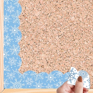 May include: Blue scalloped border with a white snowflake pattern. The border is being applied to a cork board.