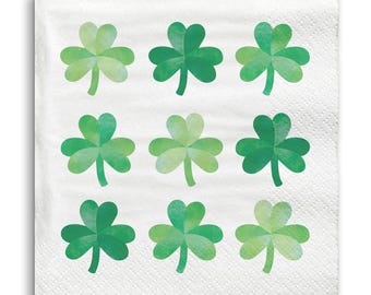 May include: White square paper napkin with a repeating pattern of nine green shamrocks. The shamrocks are in varying shades of green, creating a watercolor effect. The napkin has a subtle, textured surface.