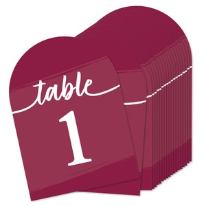 May include: Burgundy red table number cards with white brushstrokes and the text "table 1" in white. The cards are stacked in a pile.