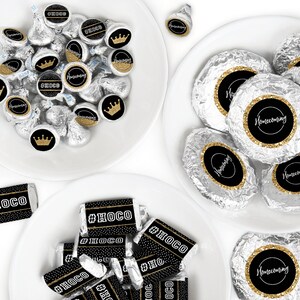 May include: A plate of chocolate kisses wrapped in silver foil with black and gold labels that say "#HOCO" and "Homecoming".  Another plate has chocolate bars wrapped in silver foil with black and gold labels that say "#HOCO".