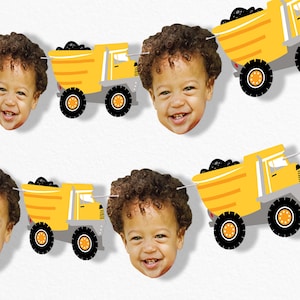 May include: A festive banner featuring smiling children's faces interspersed with yellow dump truck cutouts. The trucks are filled with black material and have black and orange wheels. The banner is strung on a white string.