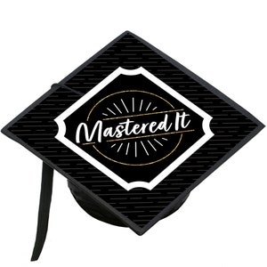 May include: Black graduation cap with a white and gold design. The design features a circle with the text "Mastered It" inside. The circle is surrounded by a white diamond shape.