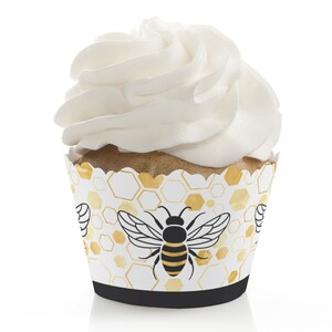 May include: White cupcake with white frosting and a black and yellow bee design on the cupcake liner. The liner has a honeycomb pattern in gold and white.